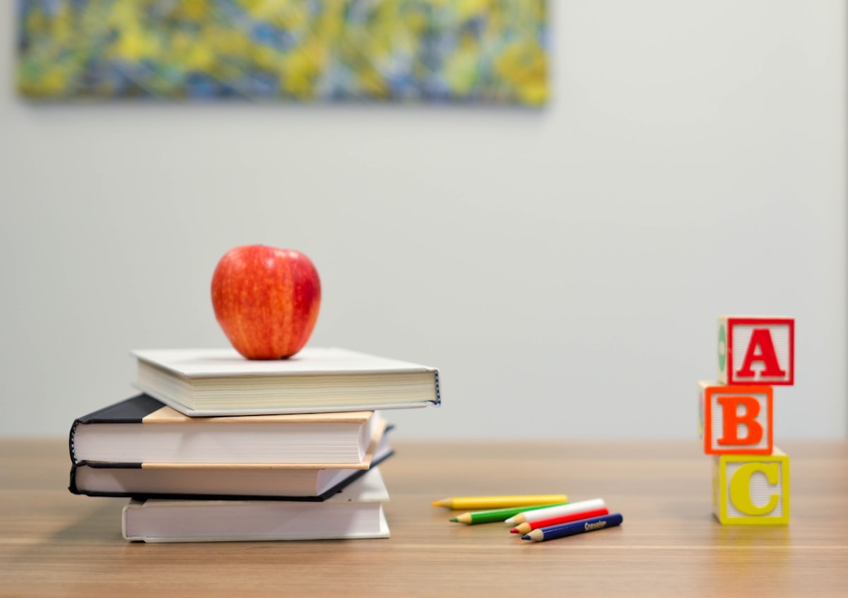 Stacked school books, coloured pencils and alphabet blocks on a desk